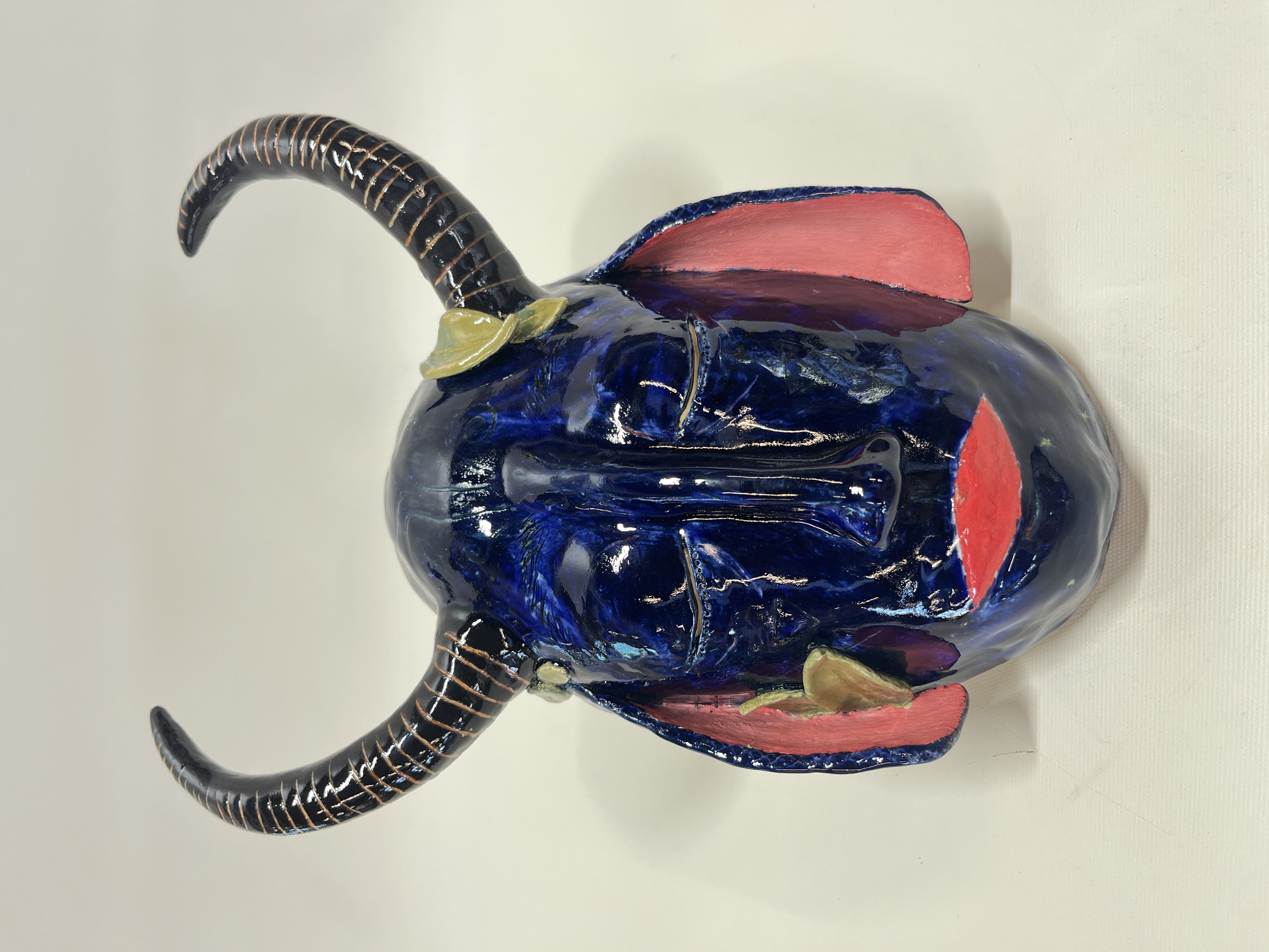 Oblong ceramic mask with curved horns, closed eyes, sheep ears, and leaves front view