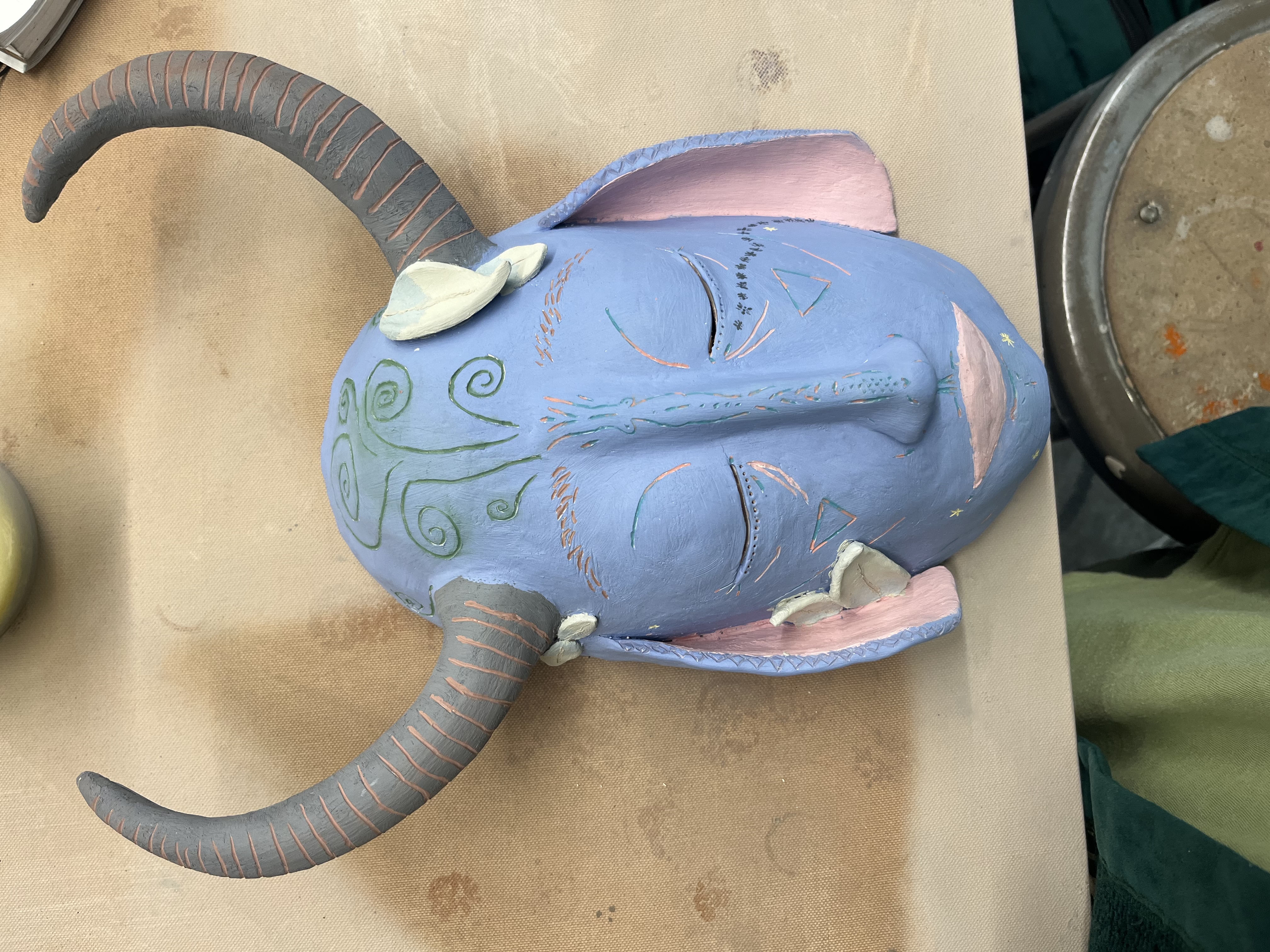 the unglazed mask reveals colorful abstract carvings and a painted line of ants down the cheek