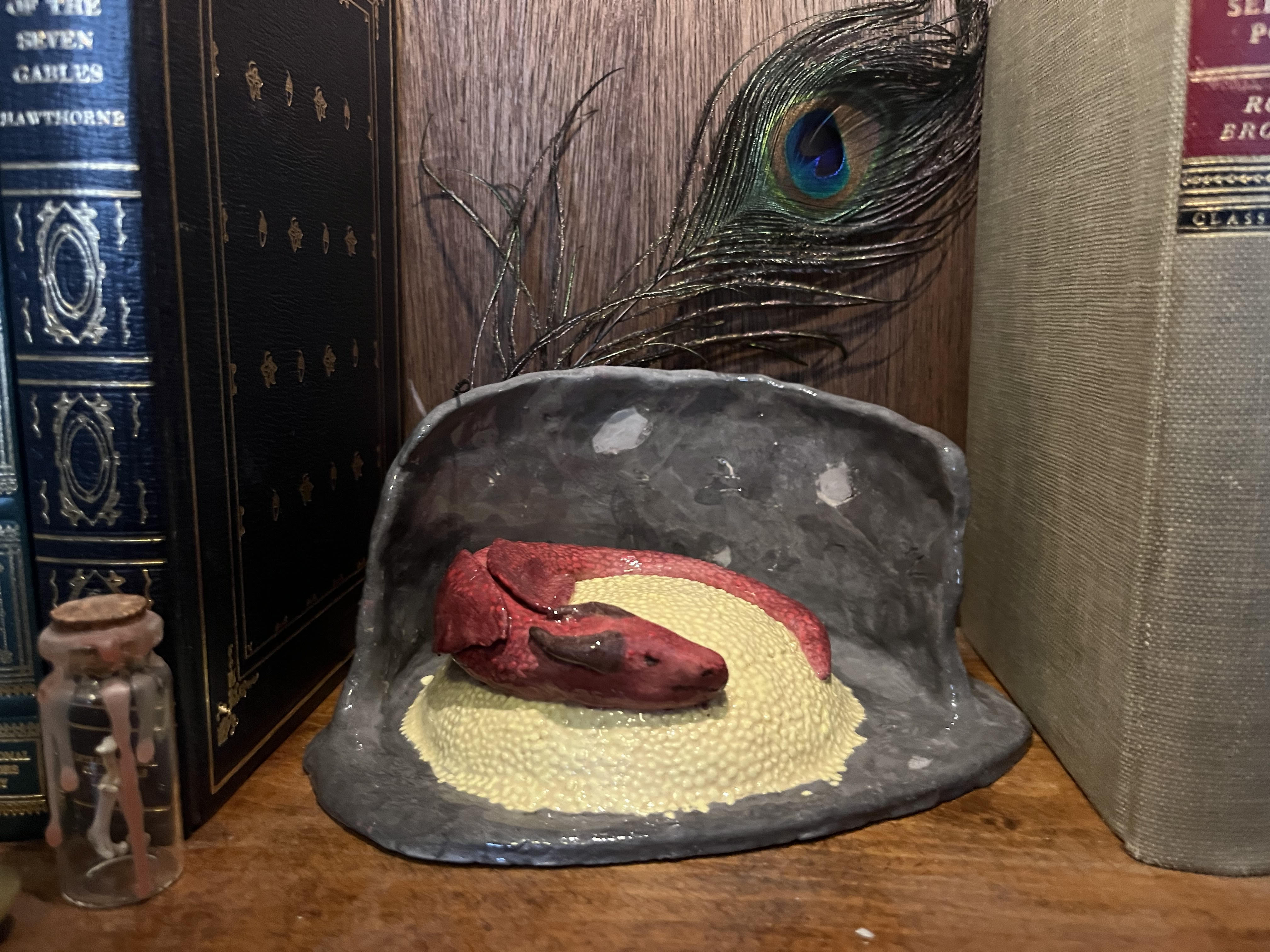 A ceramic red dragon sits atop a pile of gold in a cave