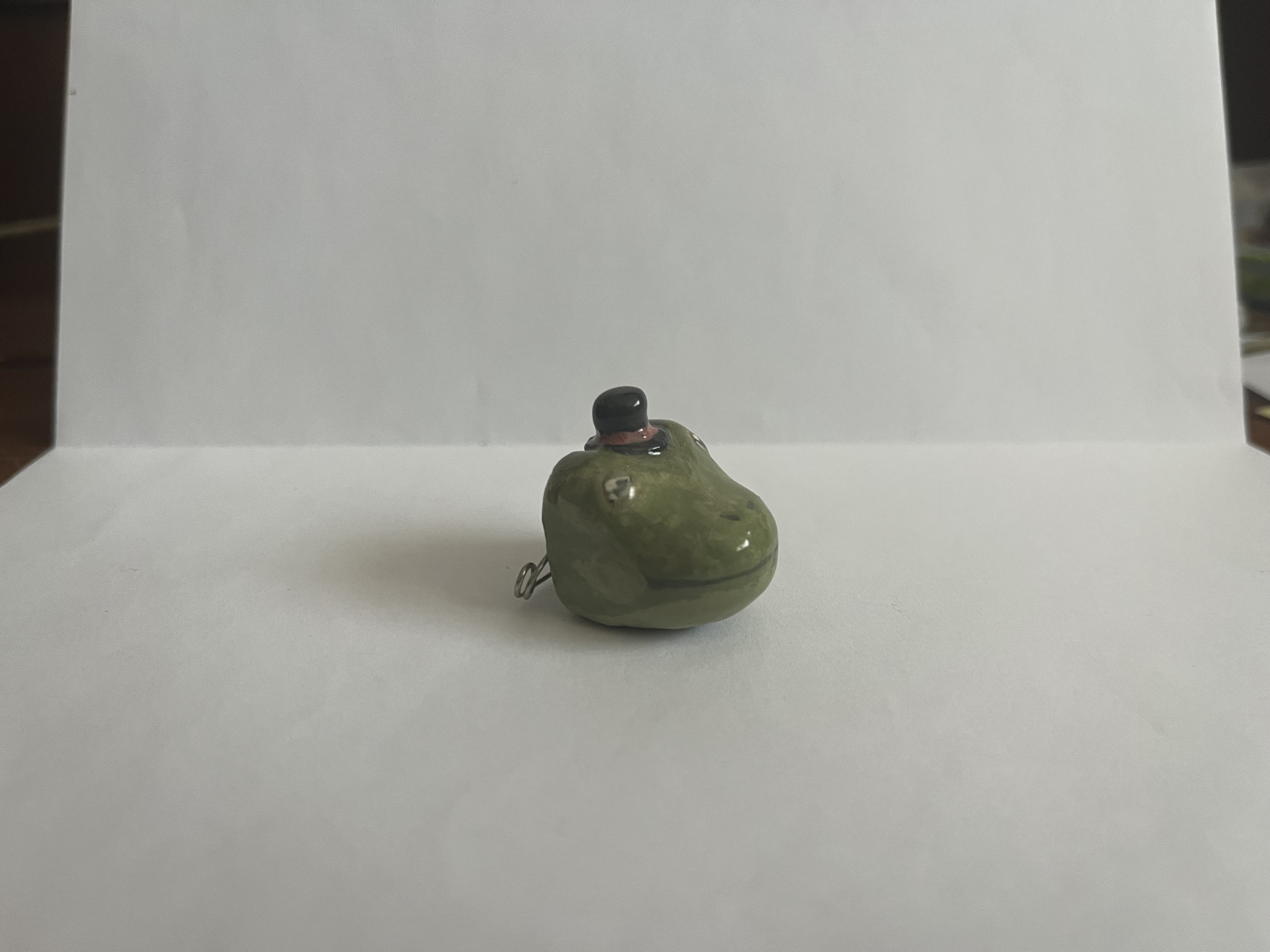 A ceramic pin of a dapper frog's head wearing a tiny top hat