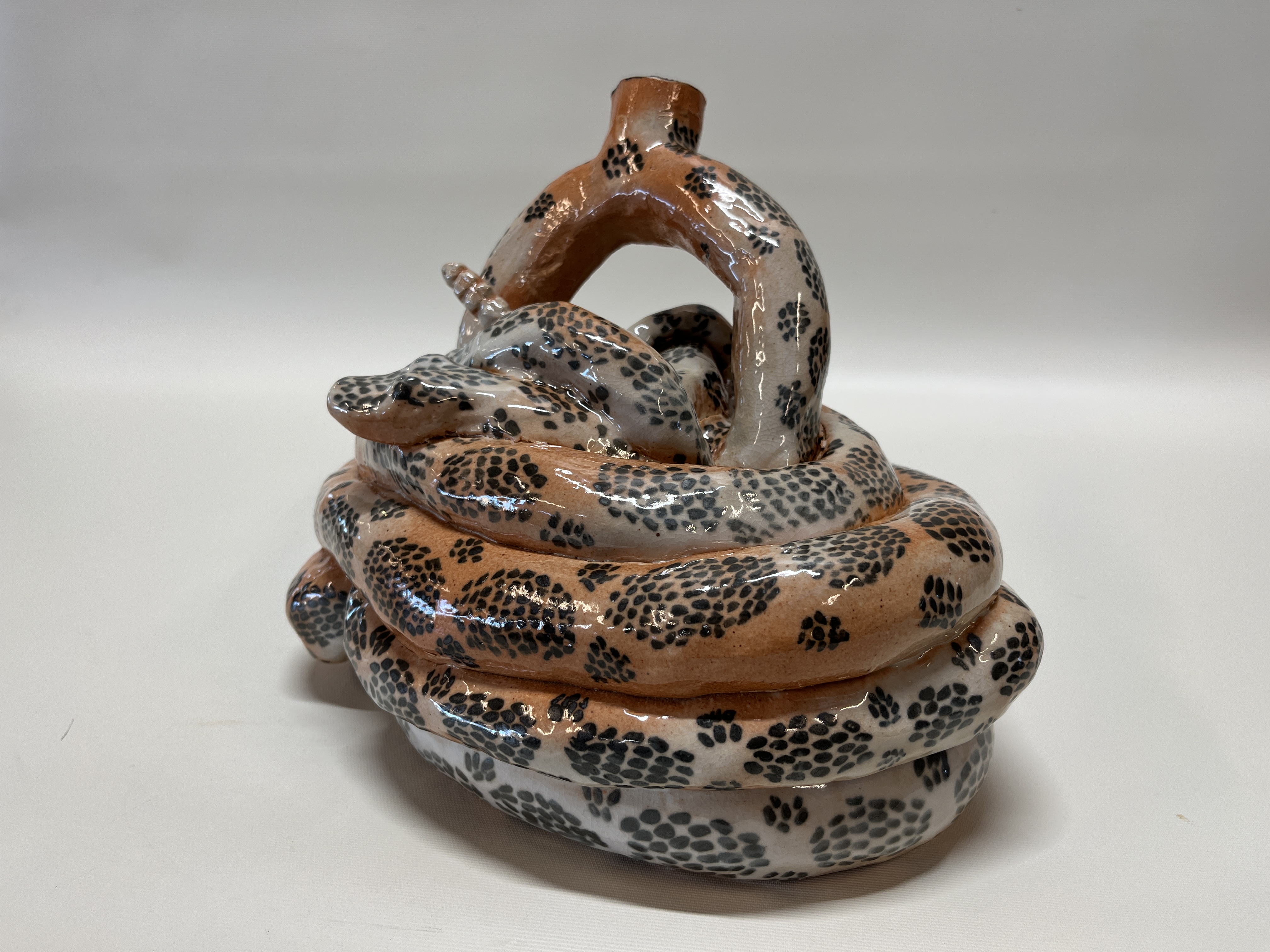 A ceramic wound rattlesnake, with a semicircle spout with a open cylindrical protrusion at the top that is also scale-patterned
