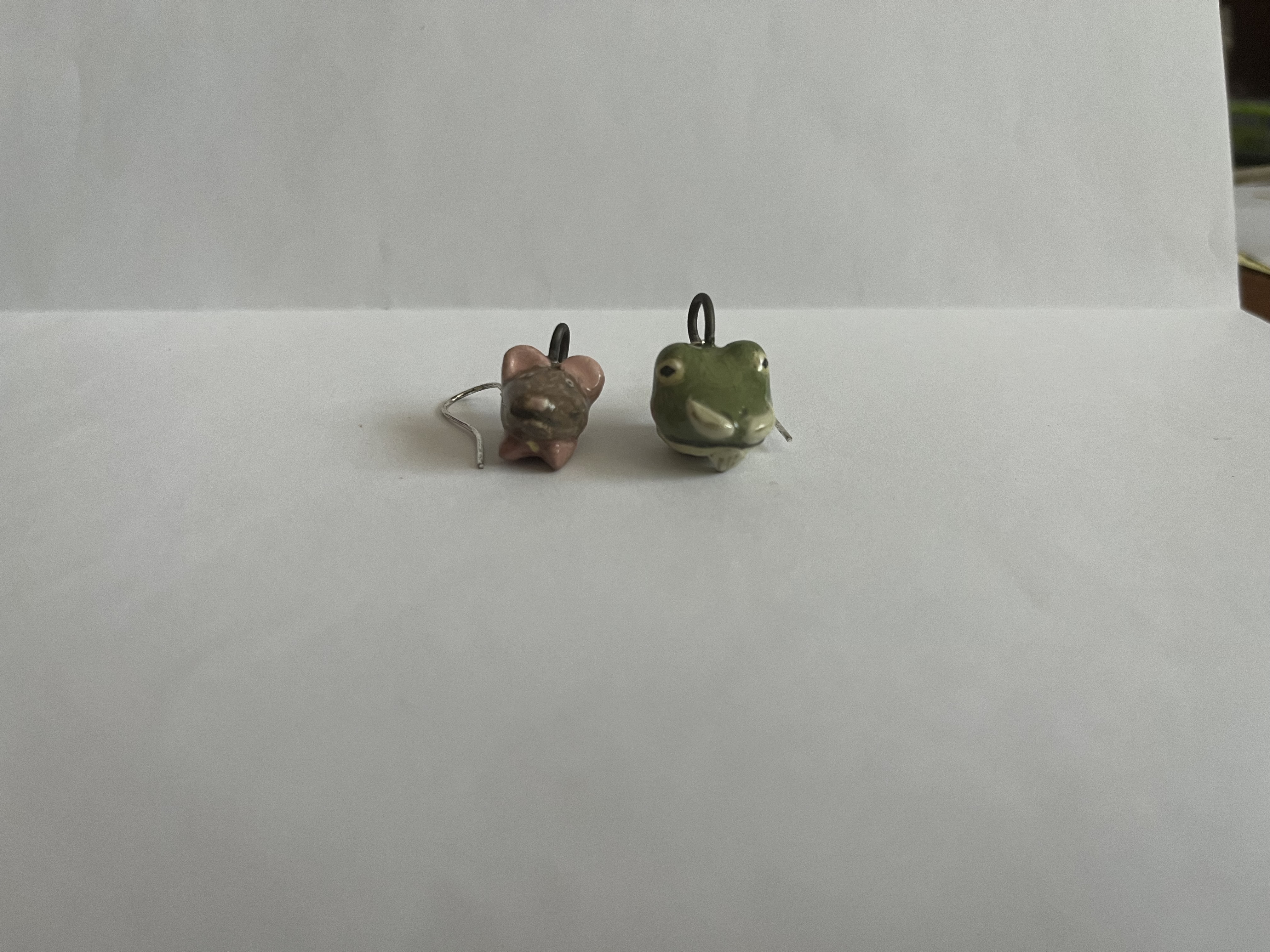 Two earrings: one is a frog's head wearing a mustache and the other is a mouse's head with a collar of a cloak